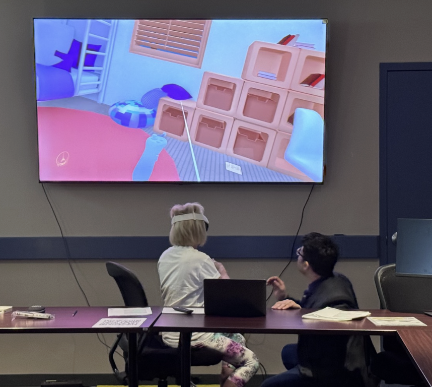 Older adult using Immersive Mind & Memory Program (IMMP) while a facilitator follows the activity on a shared display